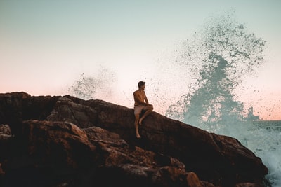 赤裸上身的男人坐在海边的岩壁上